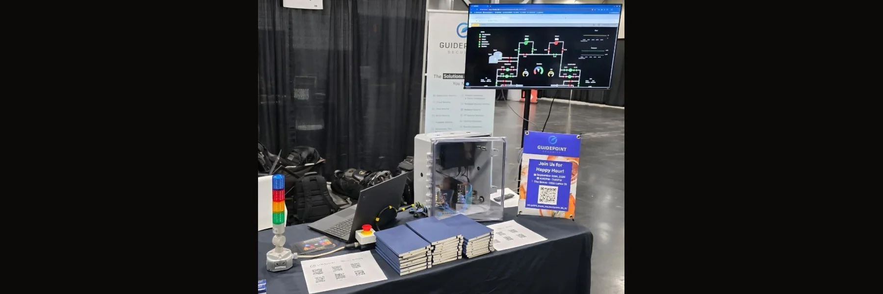 The Labshock demonstration in the GuidePoint Security booth at HOU.SEC.CON 2025 — stack light, E-Stop button and controller enclosure beside a SCADA mimic